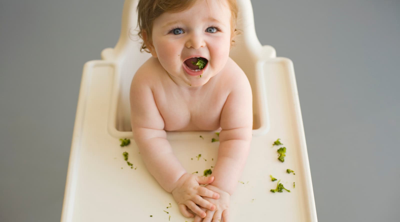 Baby sat on a baby-chair eating broccoli