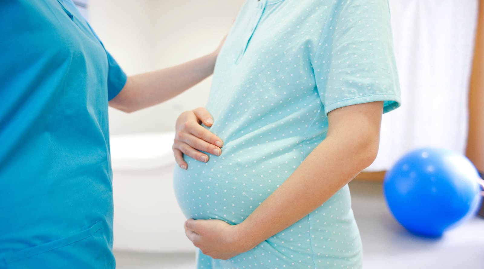 pregnant-mother-holding-baby-bump-speaking-to-nurse